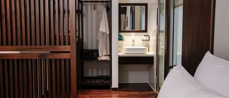 A hotel room with a wooden wardrobe, a bed, a bathroom with a sink and mirror, and a shower area.