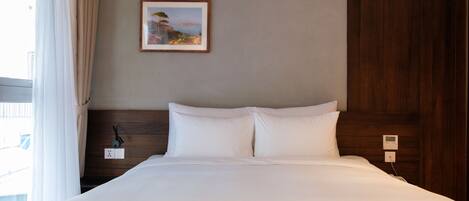 A hotel room with a bed, a nightstand, a power outlet, and a painting on the wall.