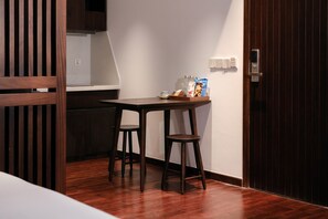 A small room with a wooden floor, a table with two chairs, a kitchen area, and a door with a handle. - Marisol Hotel (Da Nang)