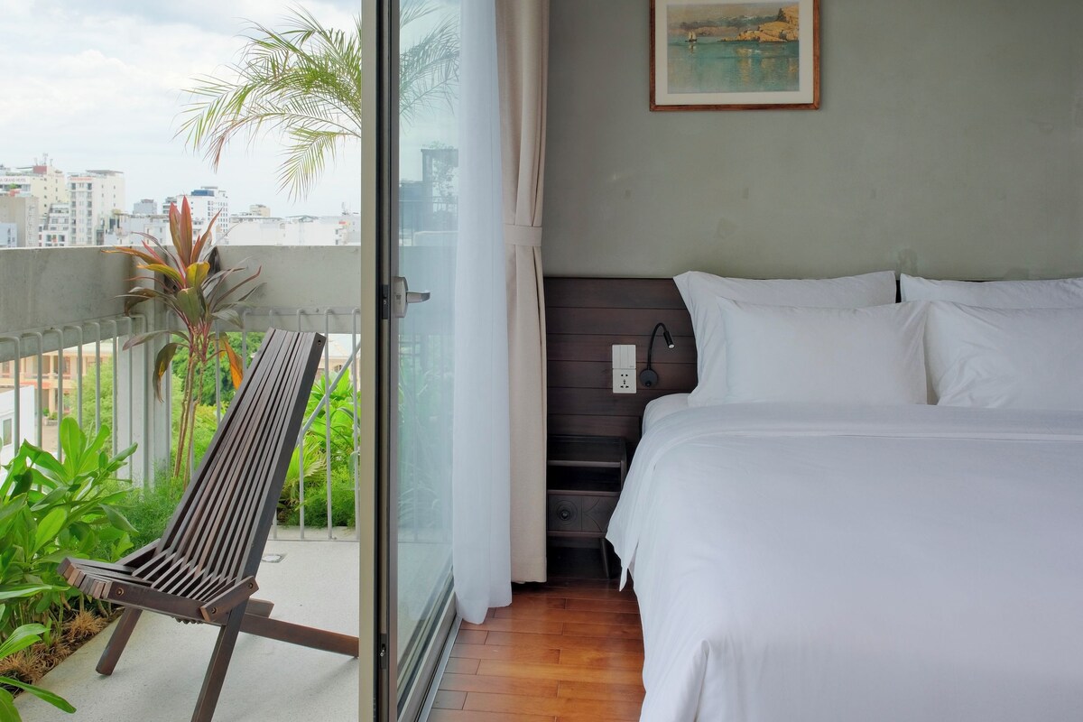 Quarto de hotel com cama, um banco e vista para a cidade.