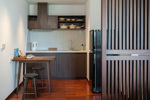 A compact kitchen with a wooden countertop, a sink, and a black refrigerator. There are stools and a small table with cups and a kettle. - Marisol Hotel (Da Nang)