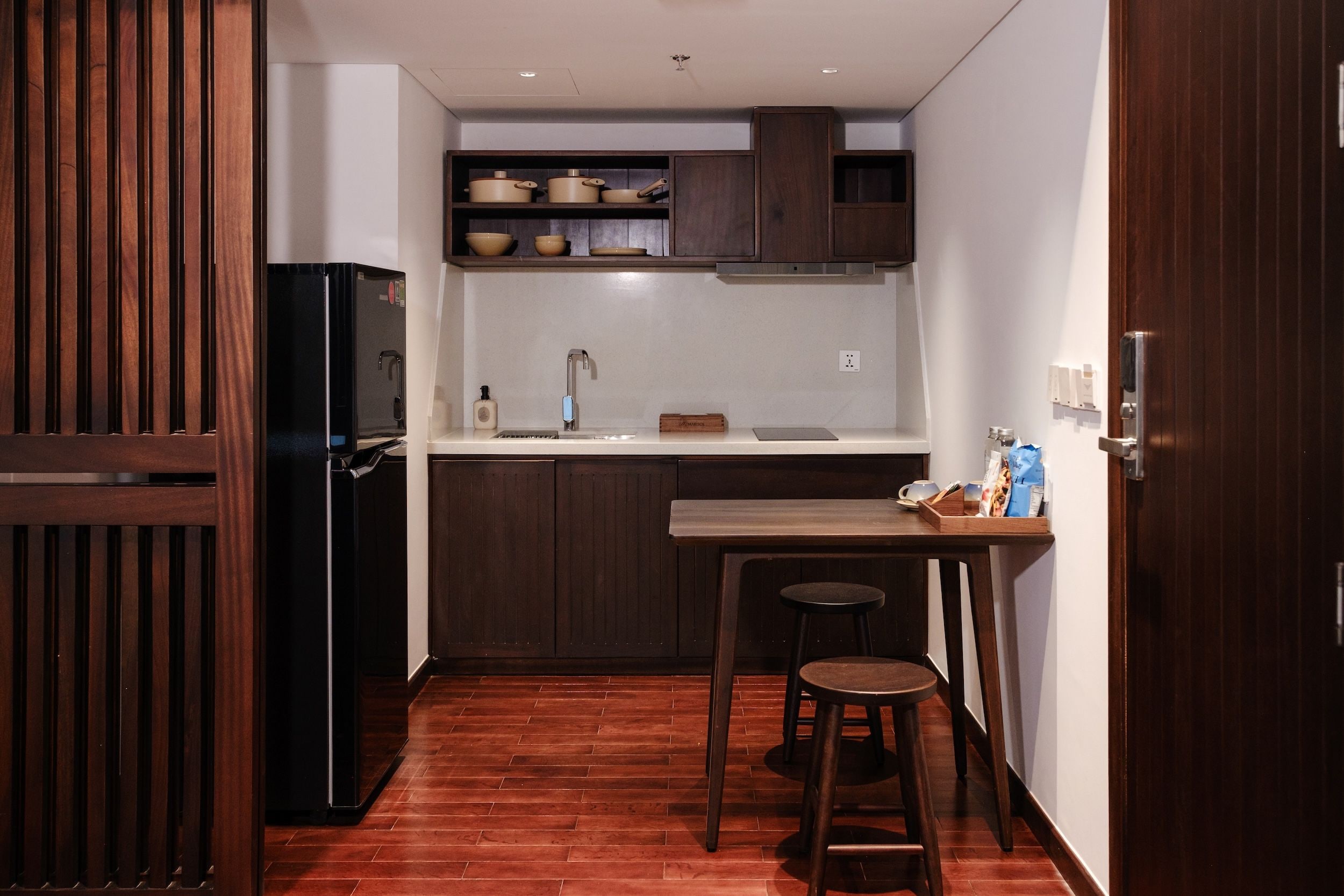Eine kleine Küche mit einem schwarzen Kühlschrank, Holzschränken, einem Spülbecken und einer Bar mit Barhocker.