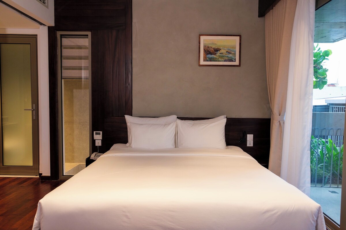 Quarto de hotel com uma cama, telefone, quadro na parede e janela com cortinas.