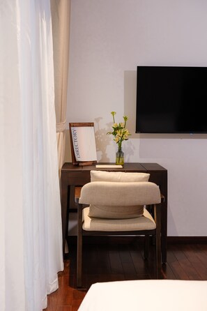 A hotel room with a bed, a desk with a flat-screen TV, a vase with flowers, and a signboard. - Marisol Hotel (Da Nang)