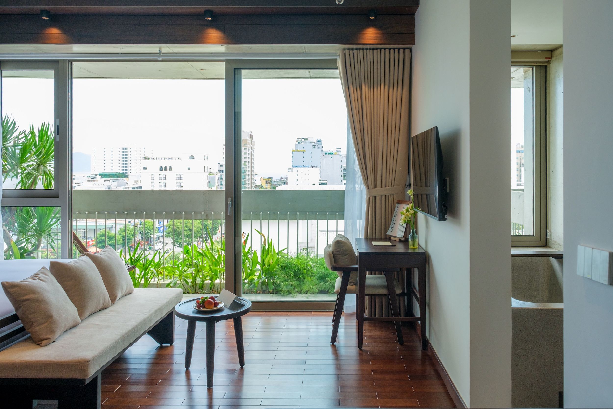 A modern living room with a sofa, a small table, and a chair. There is a large window with a view of the city.