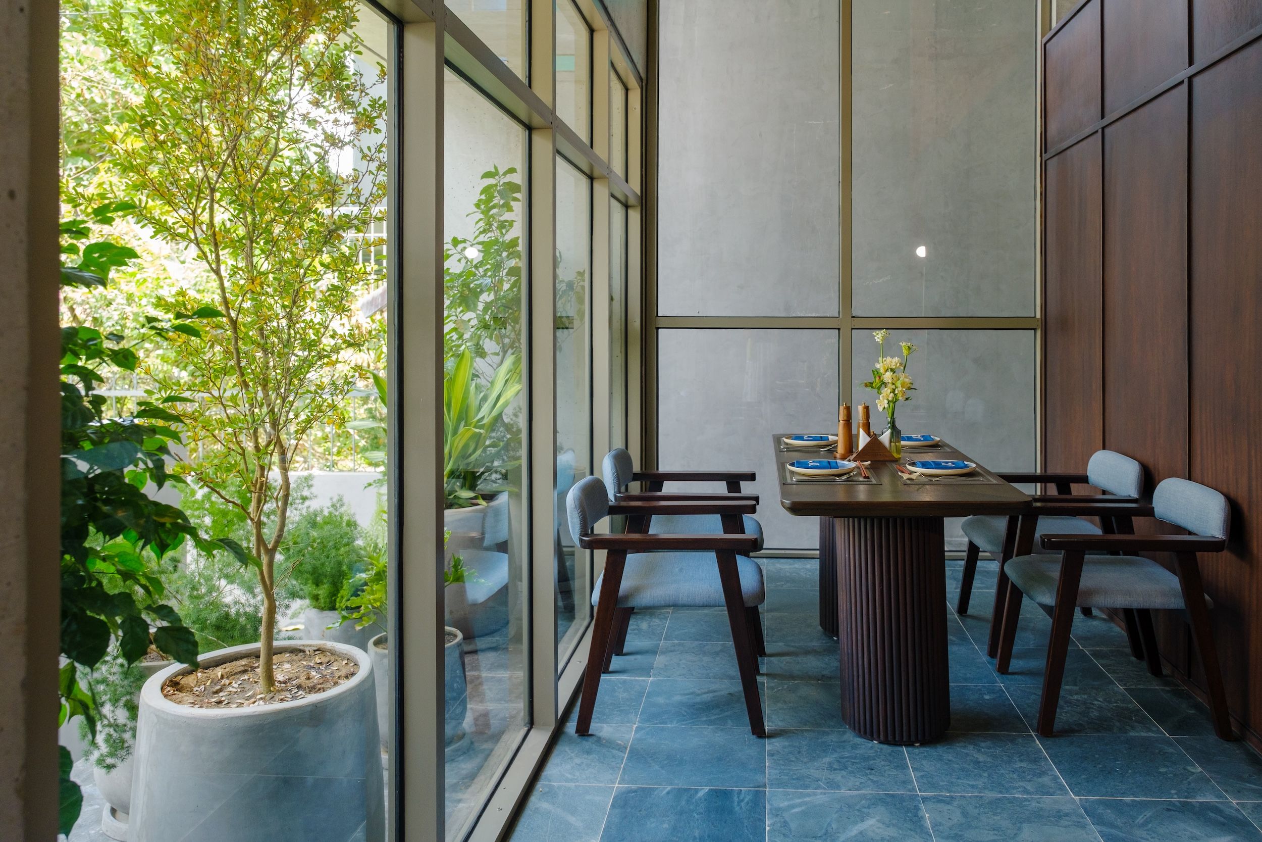 A modern dining area with a large table, chairs, and potted plants.