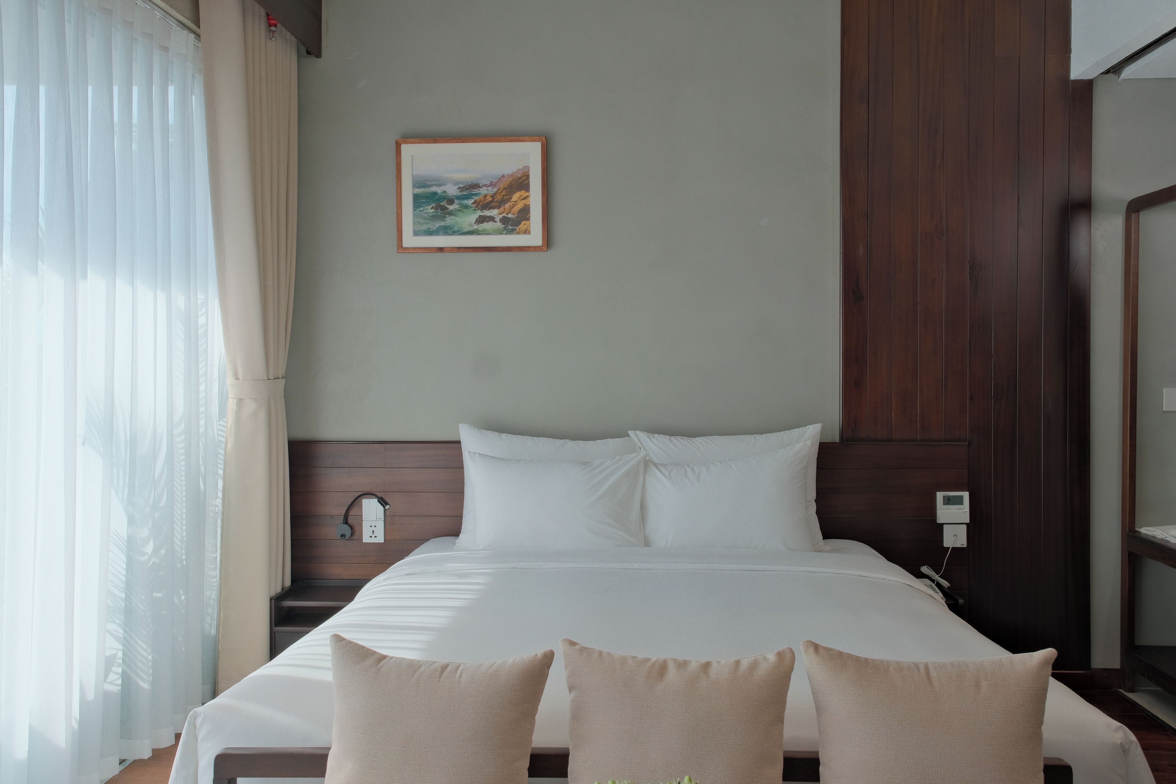 A hotel room with a bed, a painting on the wall, and a window with curtains.