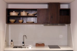 A kitchen with a white countertop, a sink, and a wooden cabinet above it. - Marisol Hotel (Da Nang)