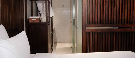 A hotel room with a bed, a wooden wardrobe, a glass shower enclosure, and a white towel.