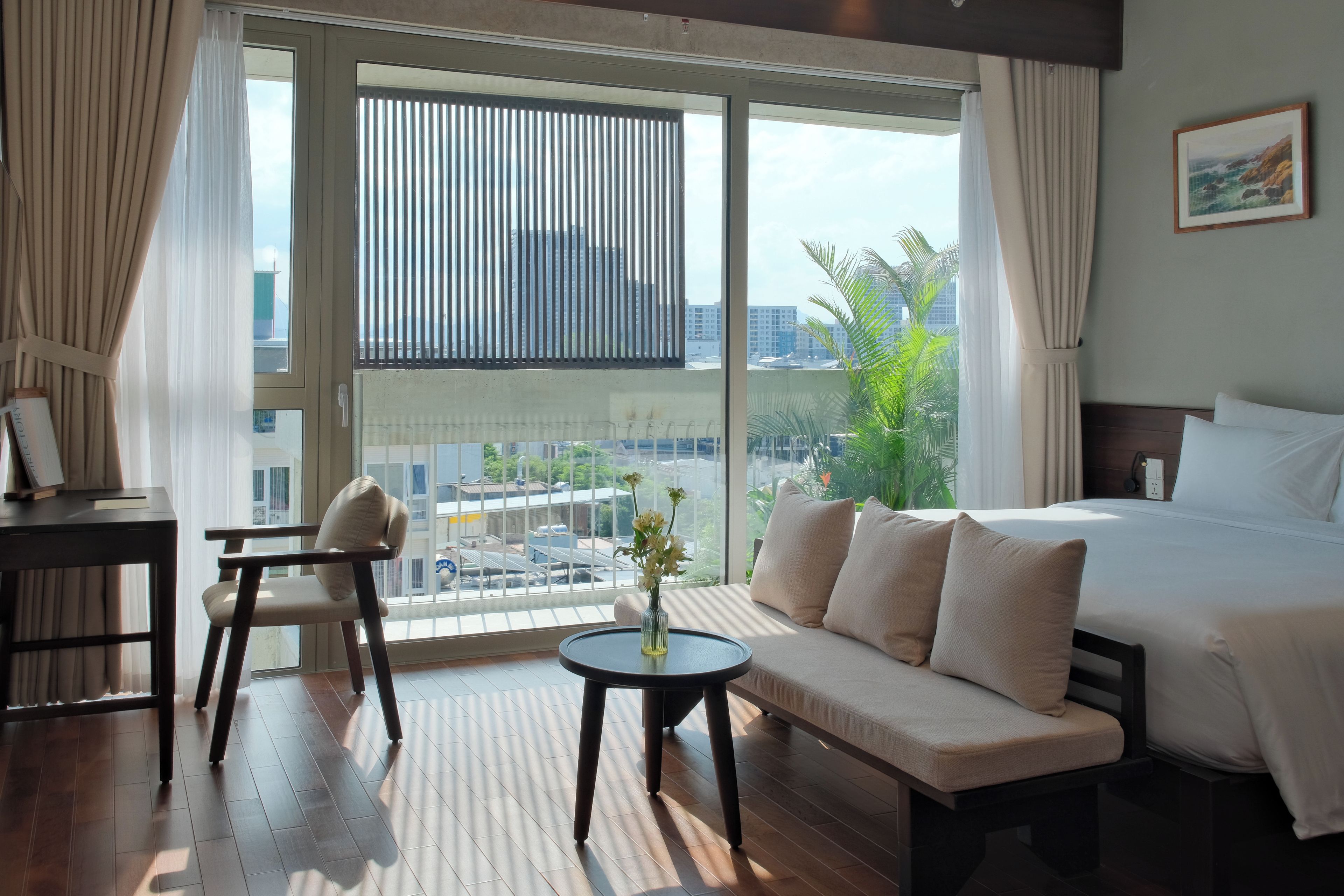 Ein Hotelzimmer mit einem Bett, einem Sofa, einem Schreibtisch und Blick auf die Stadt durch große Fenster.