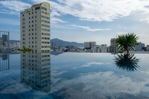 Un grand hôtel, avec son reflet net dans l’eau, entouré d’autres immeubles et avec une montagne en arrière-plan.