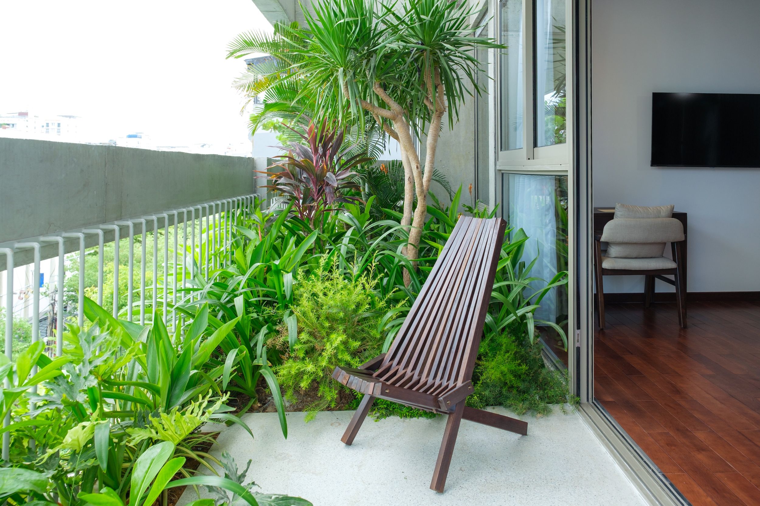 Un balcón con banca de madera, abundante vegetación y vista a la ciudad.