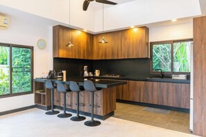 A modern kitchen with wooden cabinets, a central island with bar stools, and pendant lighting. - 3 bedrooms villa (Koh Samui)