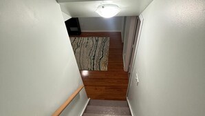 A narrow staircase with wooden steps and white walls, leading to a room with a patterned rug and a ceiling light. - Modern townhouse  offers the ideal blend of convenience and comfort, (Edmonton)