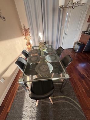A dining area with a glass-top table surrounded by chairs, a vase with flowers, and a curtain in the background. - Modern townhouse  offers the ideal blend of convenience and comfort, (Edmonton)