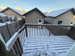 Une terrasse enneigée, dotée d’une rambarde en bois, mène à un bâtiment à l’extérieur beige et au toit en pente.