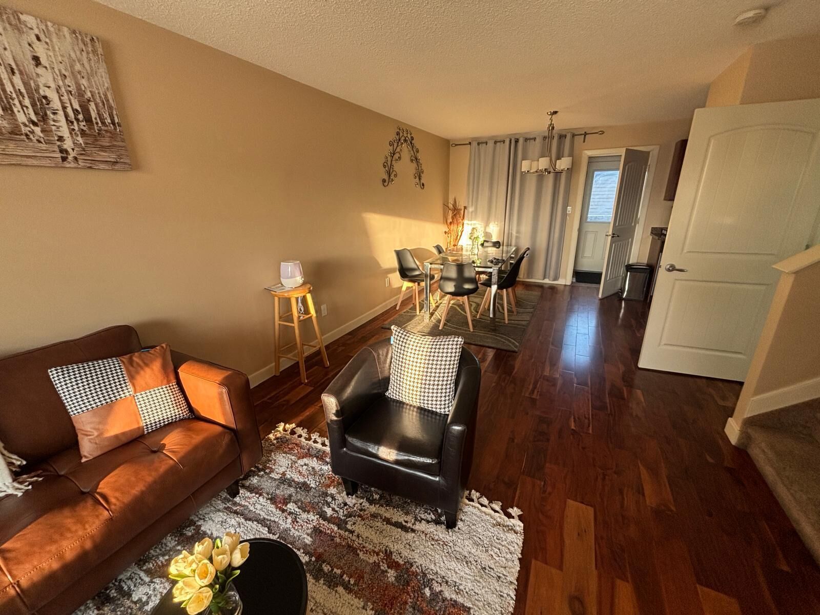 A living room with a brown leather sofa, a black leather chair, and a dining area with a glass table and chairs.