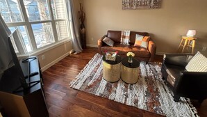 A living room with a brown leather sofa, two round coffee tables, a black armchair, and a large window with blinds. - Modern townhouse  offers the ideal blend of convenience and comfort, (Edmonton)