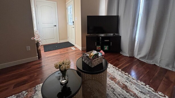 A living room with a flat-screen TV, a white door, and a small table with a vase. - Modern townhouse  offers the ideal blend of convenience and comfort, (Edmonton)