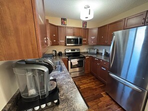 A kitchen with wooden cabinets, stainless steel appliances, a coffee maker, and a blender on the counter. - Modern townhouse  offers the ideal blend of convenience and comfort, (Edmonton)