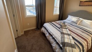 A bedroom with a bed, two windows, a view of a snowy landscape, and a painting on the wall. - Modern townhouse  offers the ideal blend of convenience and comfort, (Edmonton)