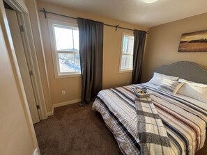 A bedroom with a bed, two windows, a view of a snowy landscape, and a painting on the wall. - Modern townhouse  offers the ideal blend of convenience and comfort, (Edmonton)
