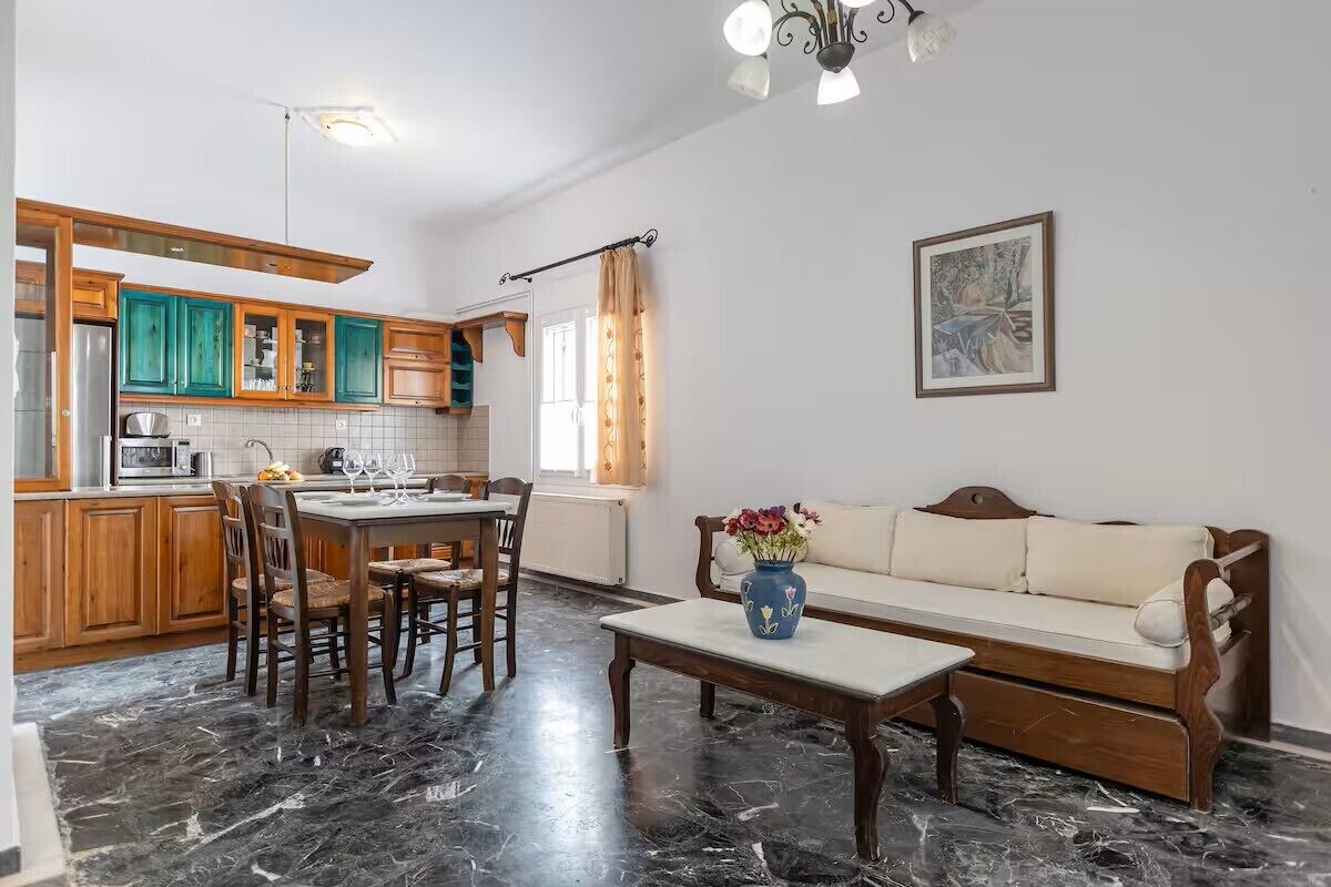 A kitchen with wooden cabinets, a dining table with chairs, a sofa, and a vase with flowers.