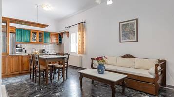 A kitchen with wooden cabinets, a dining table with chairs, a sofa, and a vase with flowers.