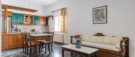 Uma cozinha com armários de madeira, uma mesa de jantar com cadeiras, um sofá e um vaso com flores.