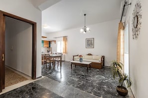 Un vaste espace de vie doté d’un sol en marbre, d’un canapé, d’une table à manger avec des chaises, et d’une cuisine à l’arrière-plan.