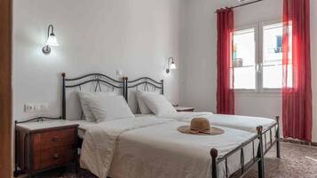A bedroom with a bed, two bedside tables, a wall-mounted lamp, a window with curtains, and a radiator.