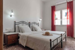 Une chambre à coucher comprenant un lit, deux tables de chevet, une lampe fixée au mur, une fenêtre avec des rideaux et un radiateur.