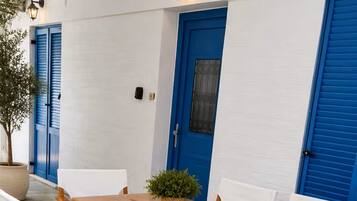 A wooden table with white chairs, a potted plant, and a blue door in a white-walled room.