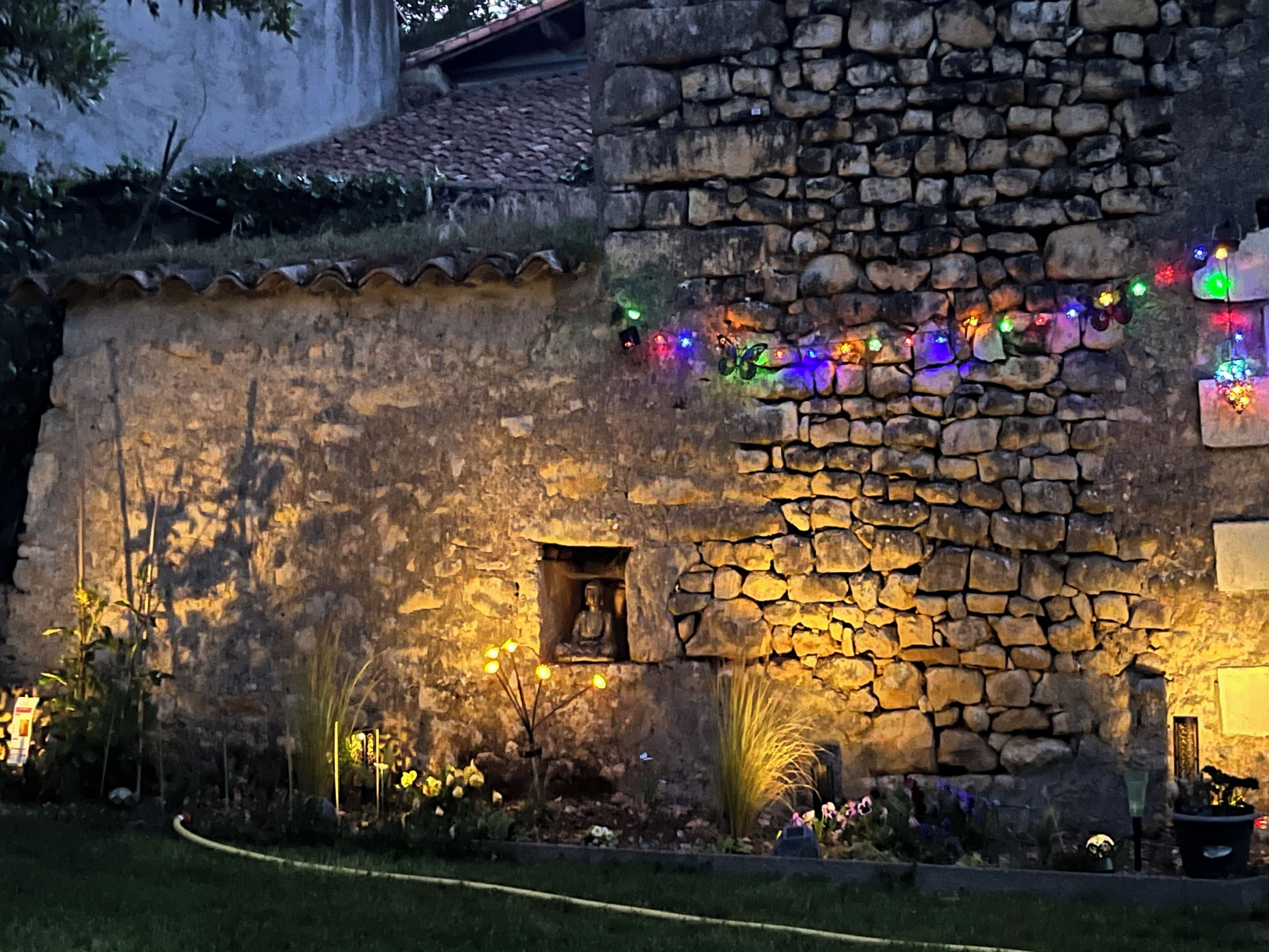 Un bâtiment en pierre doté d’une petite fenêtre et d’une porte, décoré de guirlandes lumineuses colorées.