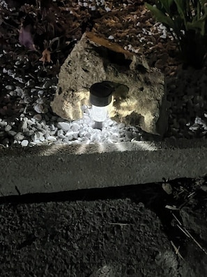 A stone structure with a light fixture embedded in it, surrounded by gravel and plants.