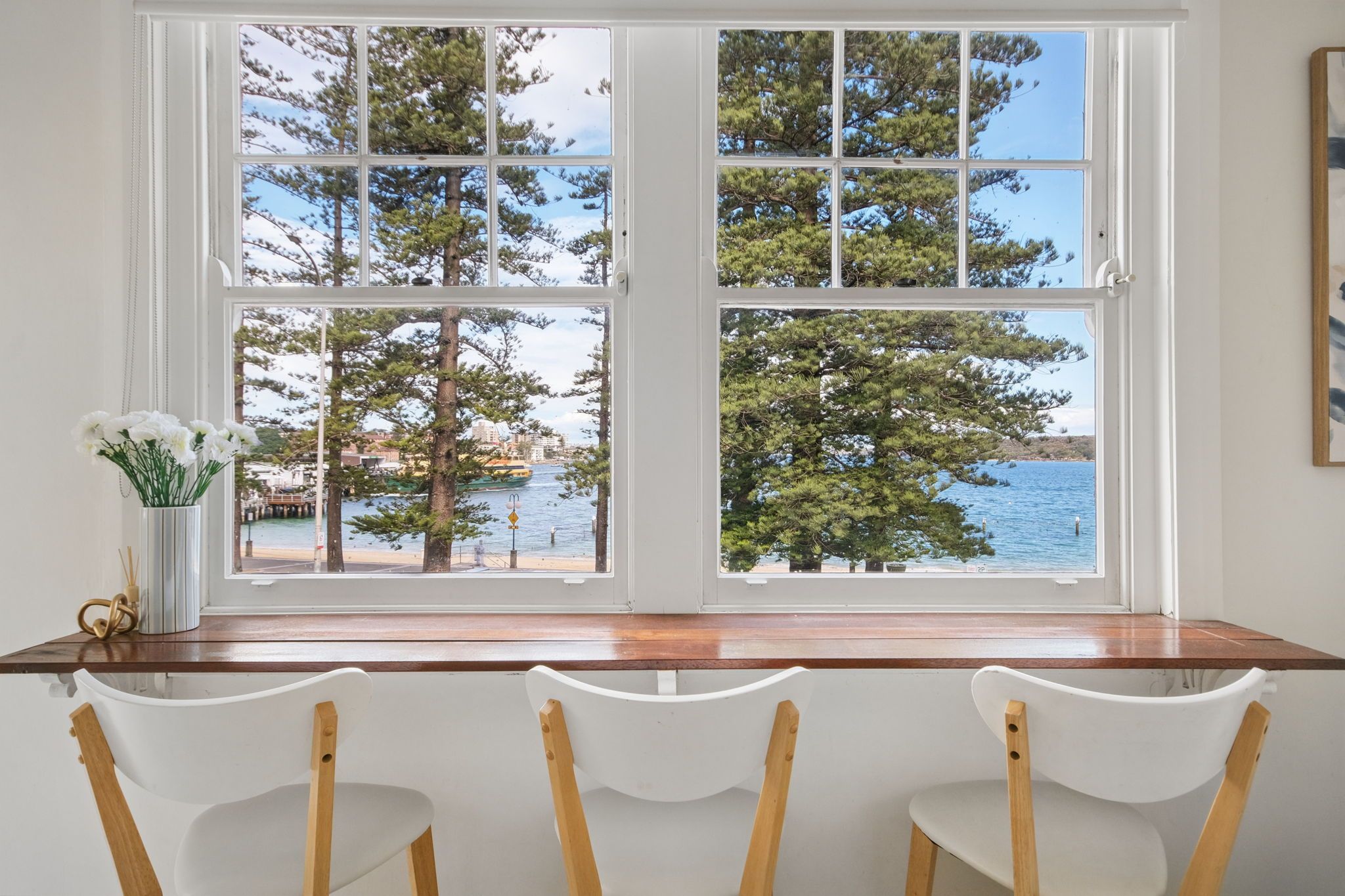 A dining area with a view of the sea and trees through a large window.