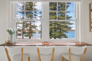 Ein Essbereich mit Blick auf das Meer und Bäume durch ein großes Fenster.