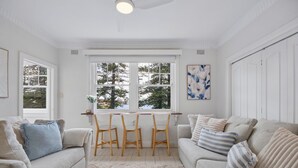 Un accogliente soggiorno con un divano bianco, un tavolino da caffè e un tavolo da pranzo con sedie. Una grande finestra offre vista su alberi e sullo skyline della città.