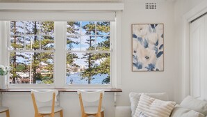 Una stanza con vista su alberi e acqua attraverso ampie finestre, un divano bianco con cuscini a righe e un quadro appeso al muro.