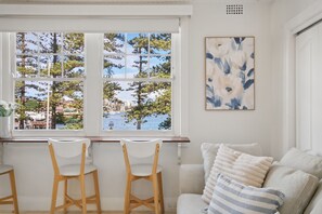 Ein Zimmer mit Blick auf Bäume und Wasser durch große Fenster, ein weißes Sofa mit gestreiften Kissen und ein Gemälde an der Wand.