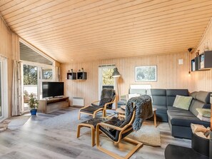 Un salon moderne avec un plafond en bois, un téléviseur à écran plat, des fauteuils en cuir, un canapé et une cheminée.