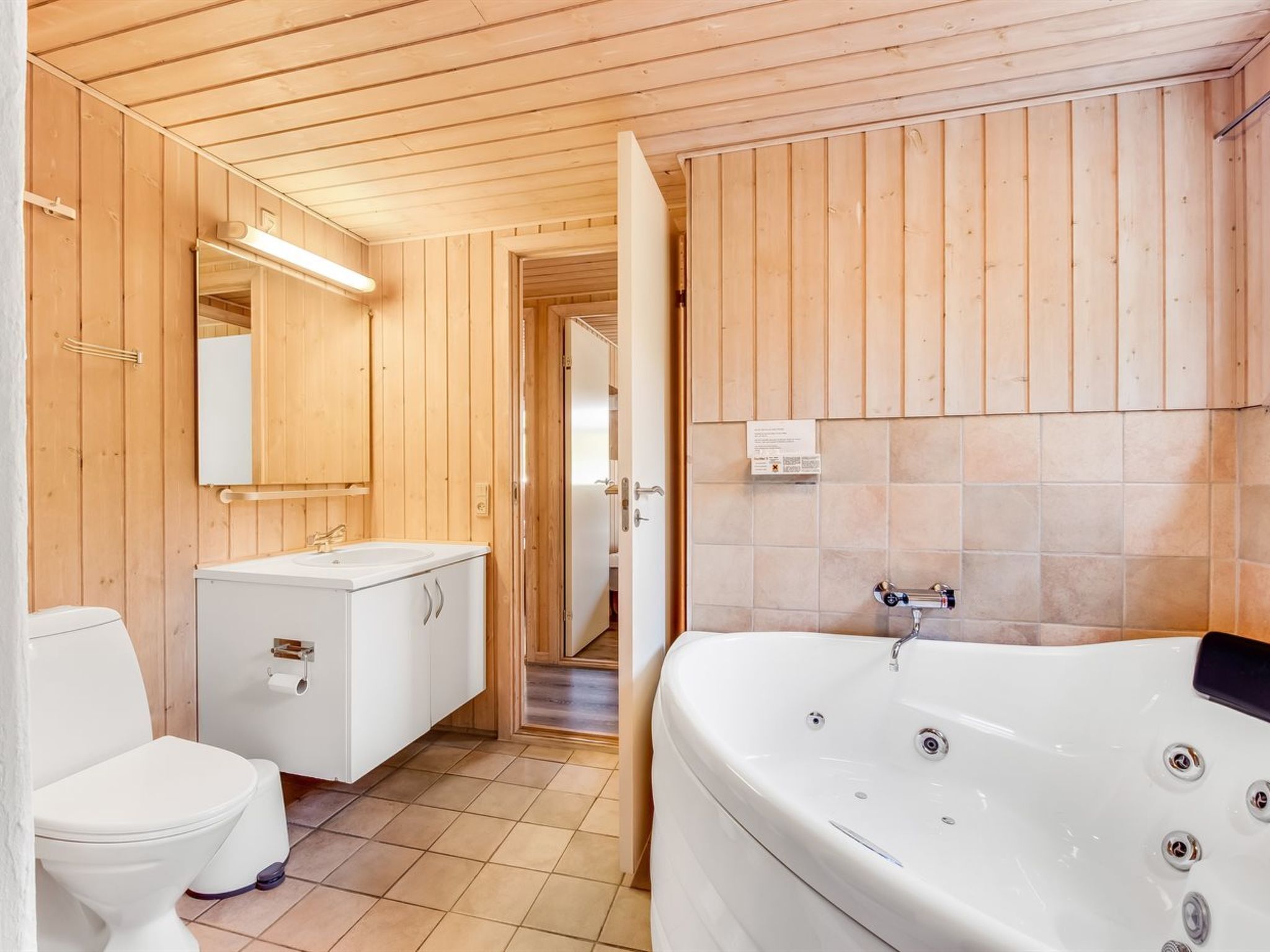 Un baño con paneles de madera, un lavamanos blanco, un inodoro y una bañera grande.