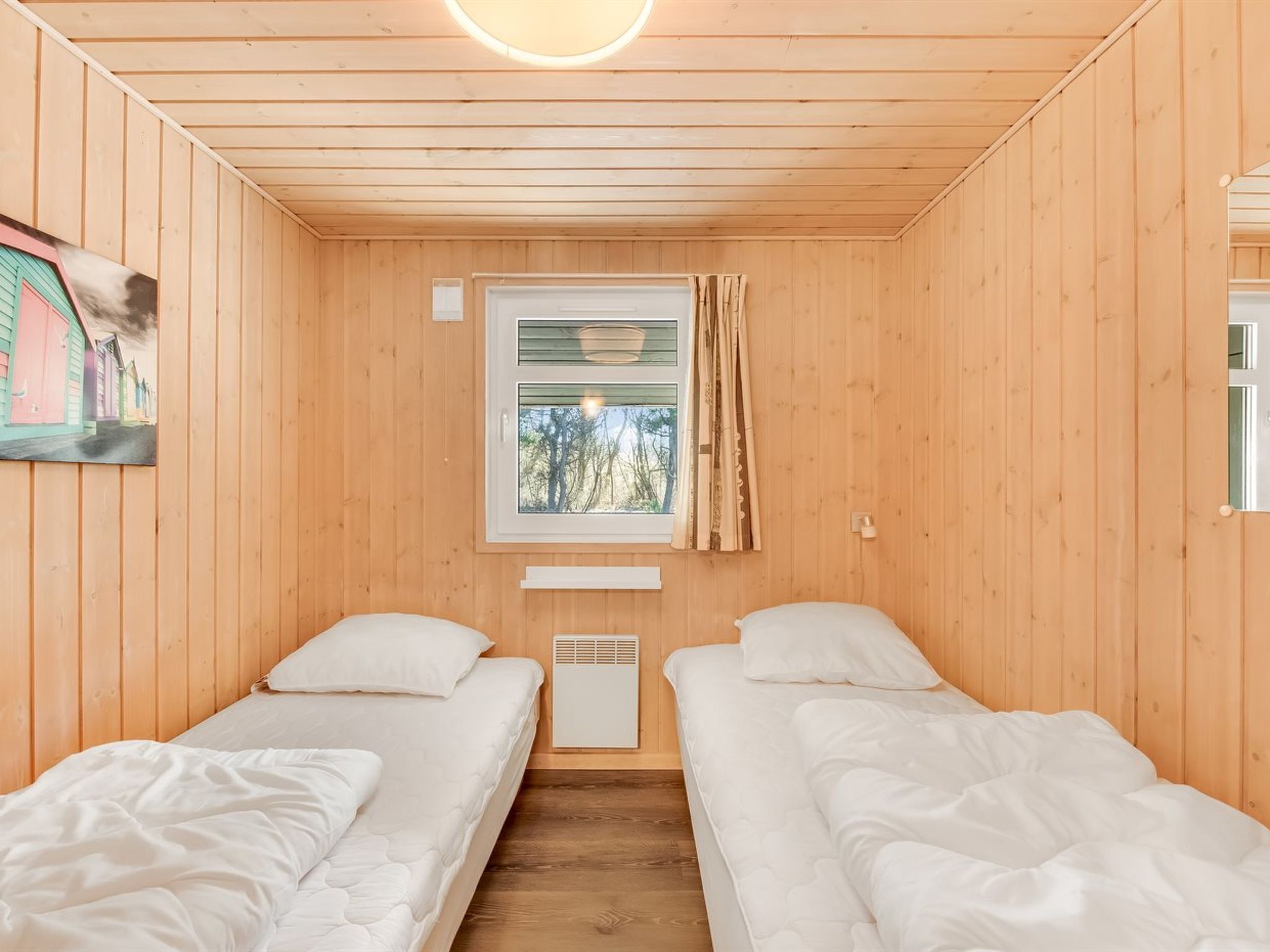 A room with two beds, a window with curtains, and a painting on the wall.