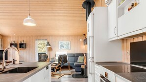 Una cocina moderna con muebles blancos, horno empotrado y un área de comedor con sofá gris y una pequeña mesa.