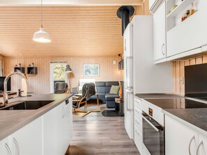 Eine moderne Küche mit weißen Schränken, einem eingebauten Ofen und einem Essbereich mit einem grauen Sofa und einem kleinen Tisch.