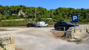Un área de estacionamiento con un letrero azul de estacionamiento, un muro de piedra y un camino de tierra.