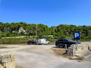 Ein Parkplatz mit blauem Parkschild, einer Steinmauer und einem Feldweg.