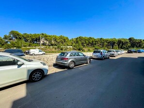 A parking lot with multiple cars parked, a stone wall, and trees in the background. - FranSea House - Otranto (Otranto)