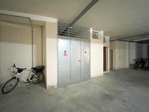 A parking garage with a white bicycle parked against a wall, a metal gate, and a motorcycle in the background. - FranSea House - Otranto (Otranto)