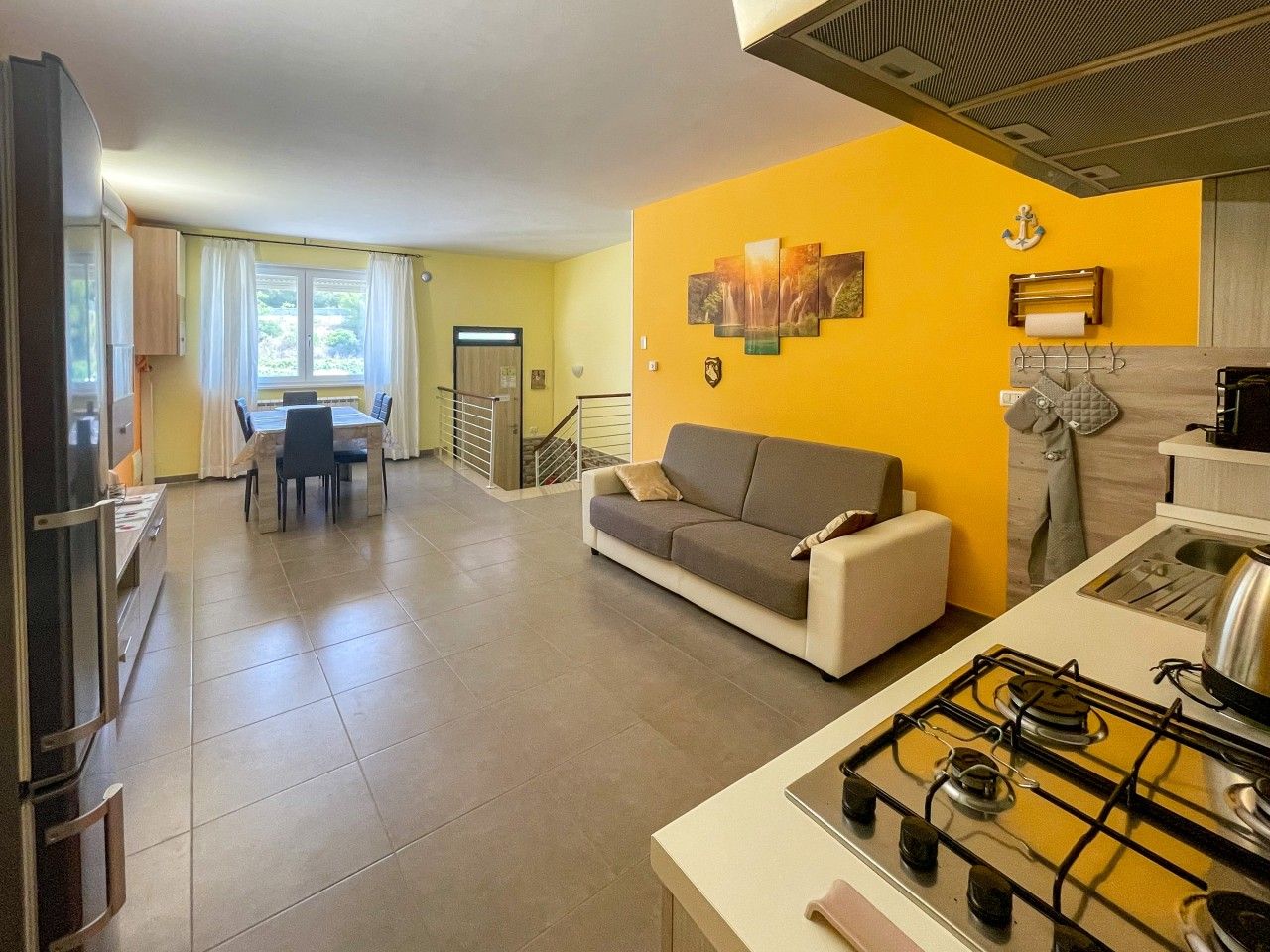 A modern kitchen with a gas stove, a dining area with a table and chairs, and a living room with a sofa.